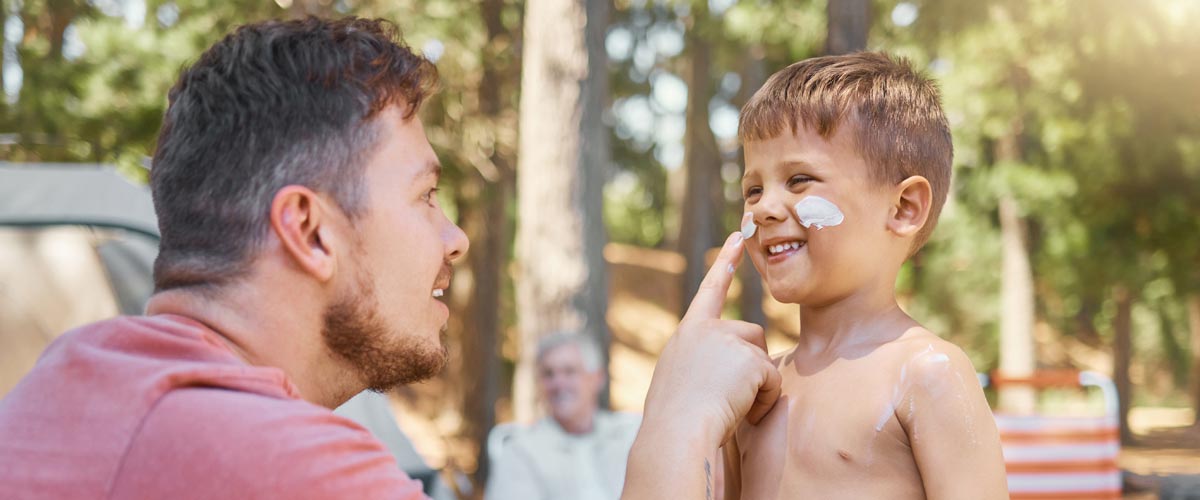 Dad applying sunscreen to son's face while camping