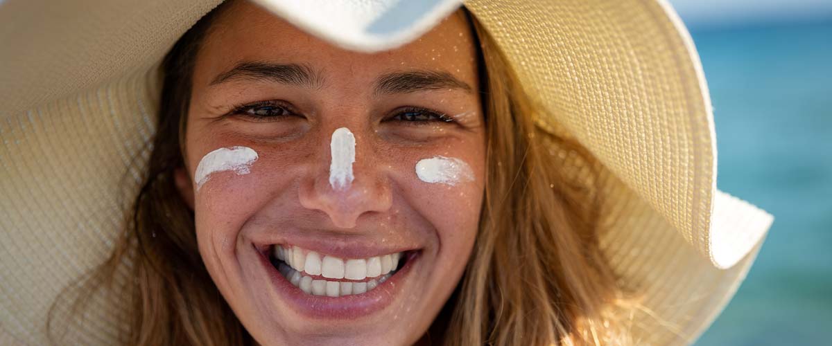 Smiling woman wearing a sun hat and sunscreen on face